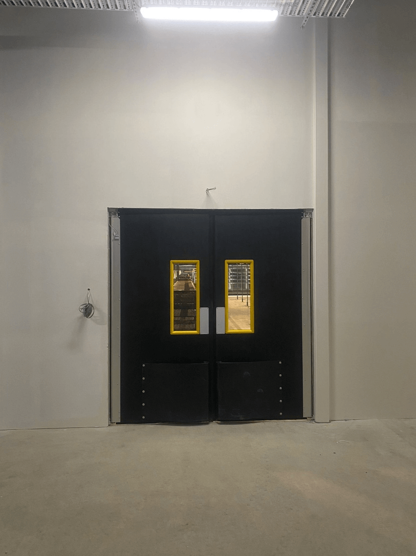 Black double swing doors with yellow-bordered windows in a warehouse setting.