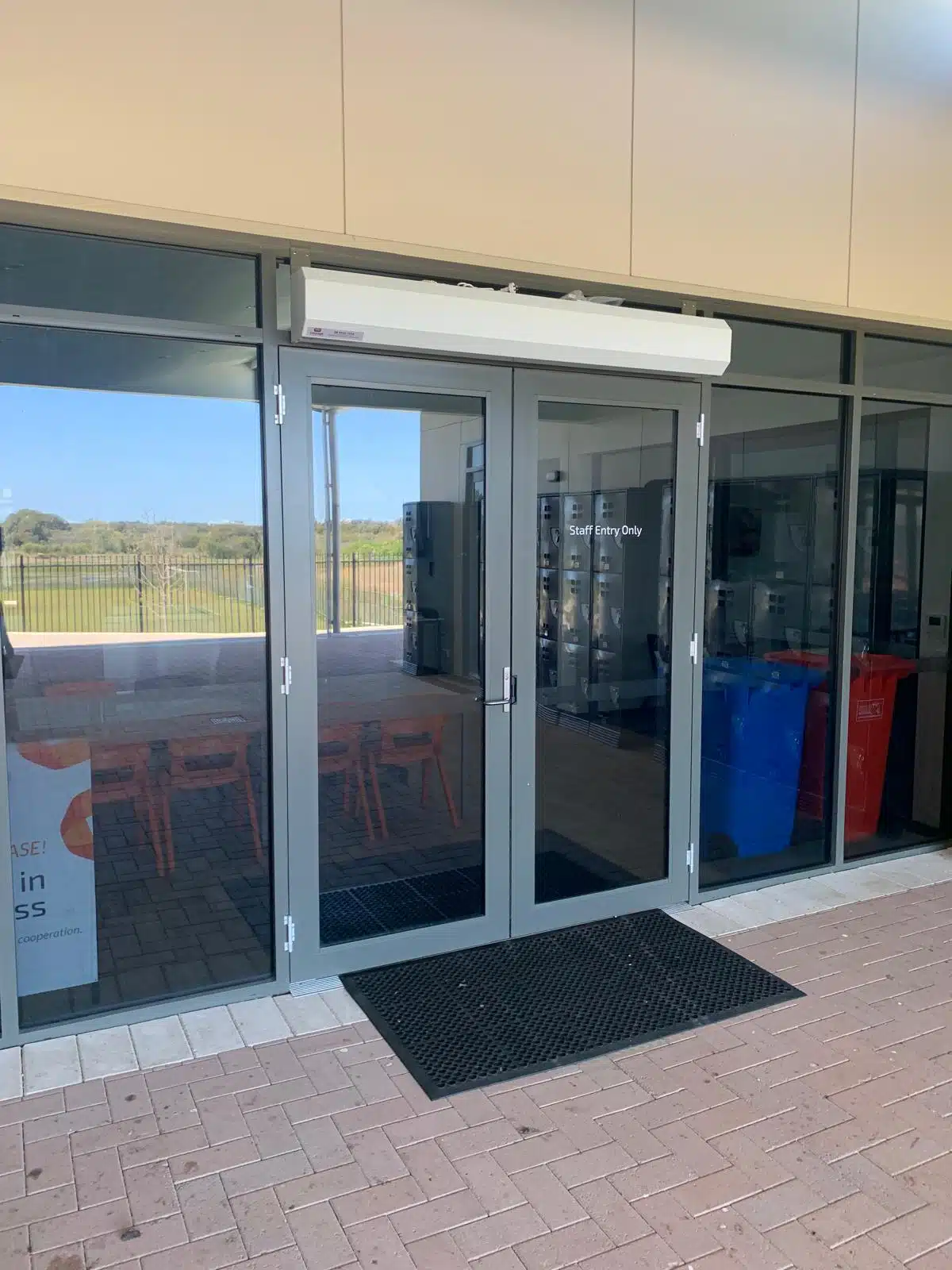Glass double doors with an air curtain installed above and a "Staff Entry Only" sign.