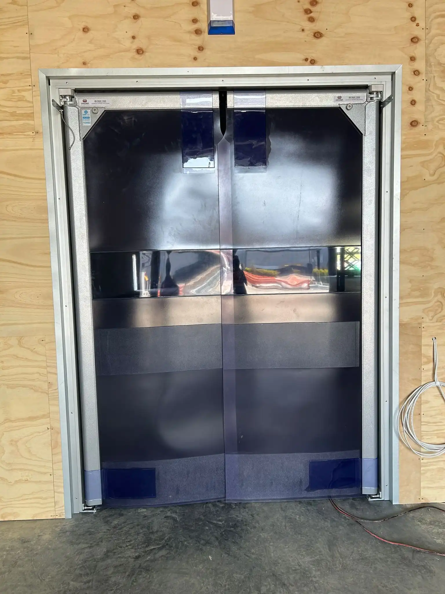 Industrial double-swing vinyl strip door installed in a plywood-framed wall.