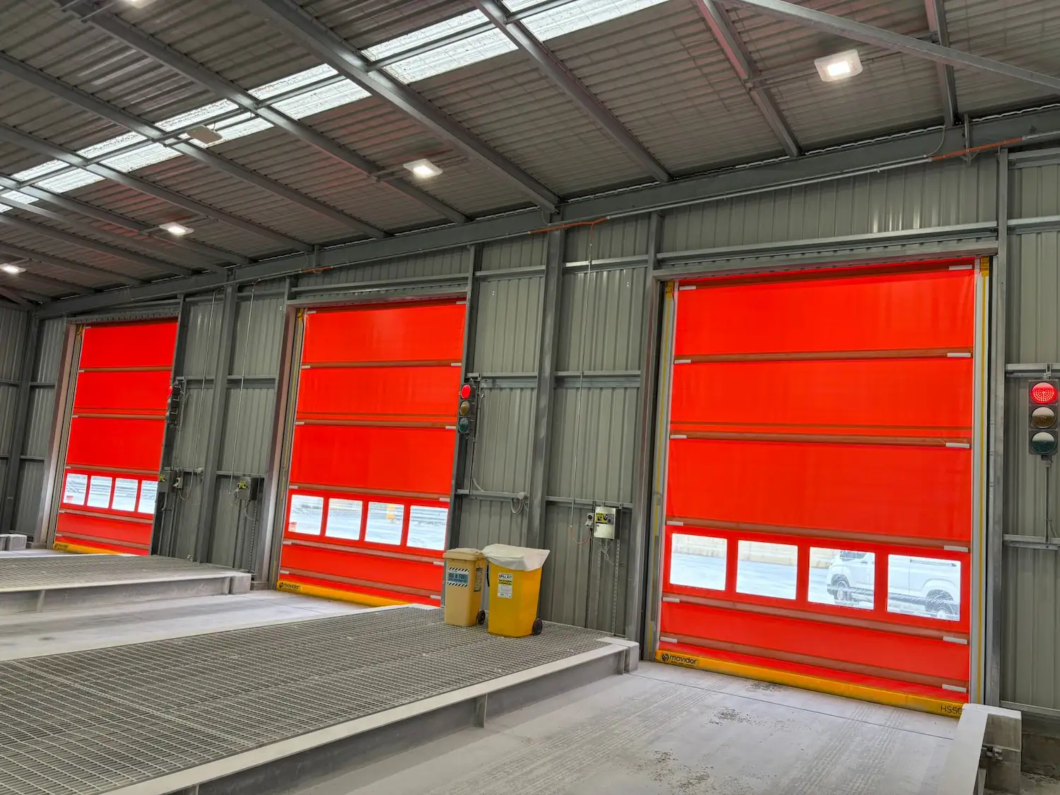 Three large orange high-speed rapid roll doors installed in a warehouse loading bay with traffic light control systems.