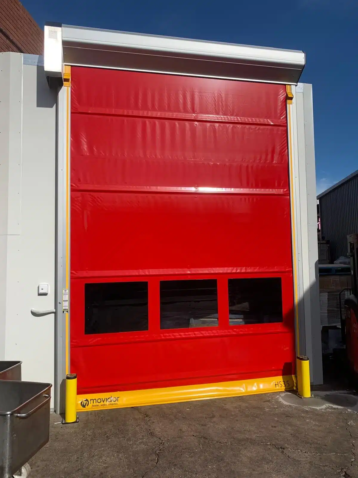 Red Movidor HS35 rapid door installed at an outdoor entrance under a clear blue sky