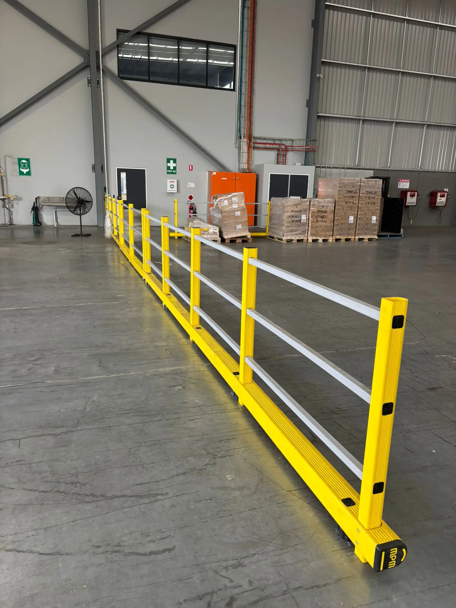 Long run of yellow DEFLEX flexible pedestrian safety barrier separating a walkway inside a warehouse