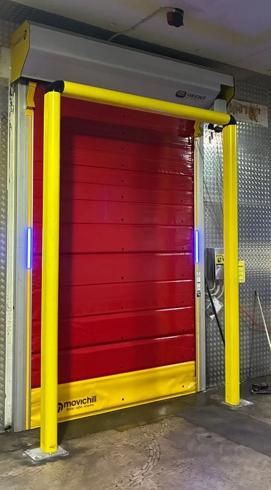 Red Movichill insulated rapid roller door with yellow base, protected by a yellow full-frame bollard at a cold storage entrance